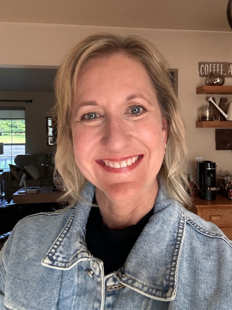 Mary Magnin smiling in her home, wearing a denim jacket.
